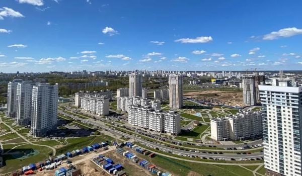 Eine Frau in schwarzem Mantel und Schal läuft Schlittschuh auf dem Eis, mit schneebedeckten Bäumen im Hintergrund.